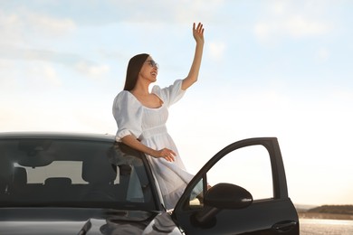 Smiling young woman in sunglasses leaning out of car outdoors. Enjoying trip