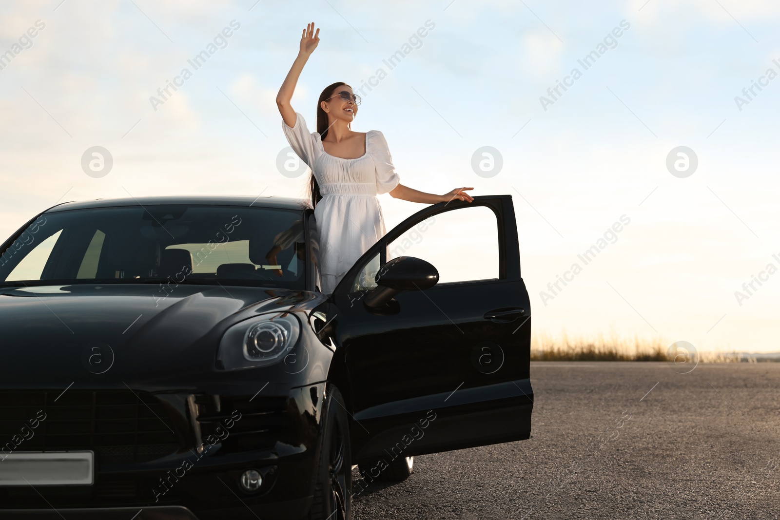 Photo of Smiling young woman in sunglasses leaning out of car outdoors. Enjoying trip