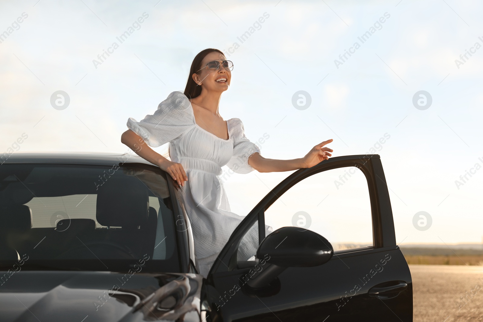 Photo of Smiling young woman in sunglasses leaning out of car outdoors. Enjoying trip