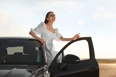 Smiling young woman in sunglasses leaning out of car outdoors. Enjoying trip