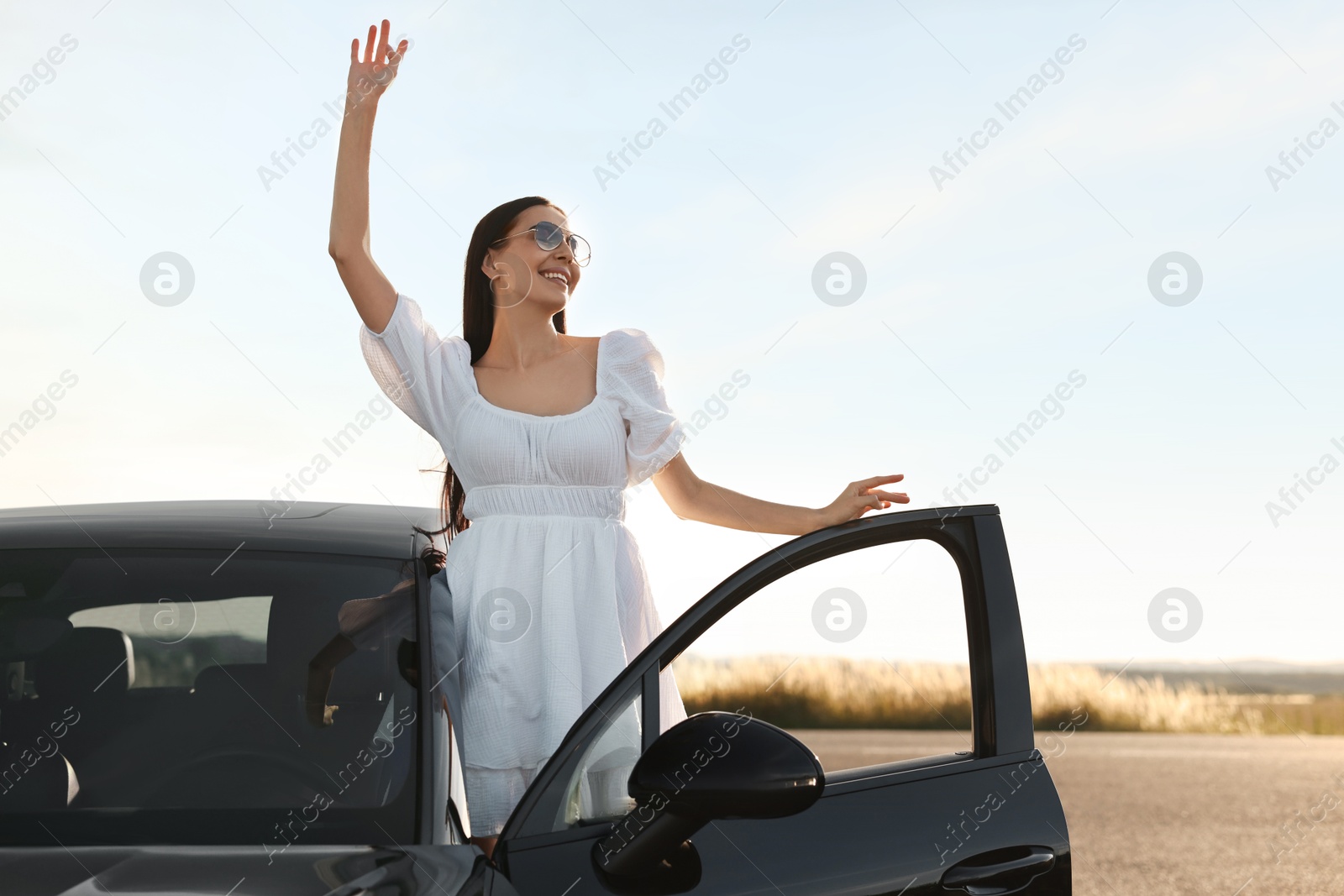 Photo of Smiling young woman in sunglasses leaning out of car outdoors. Enjoying trip