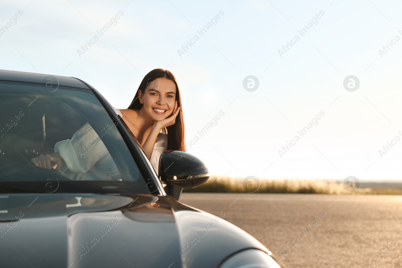 Photo of Smiling young woman leaning out of car window outdoors. Enjoying trip