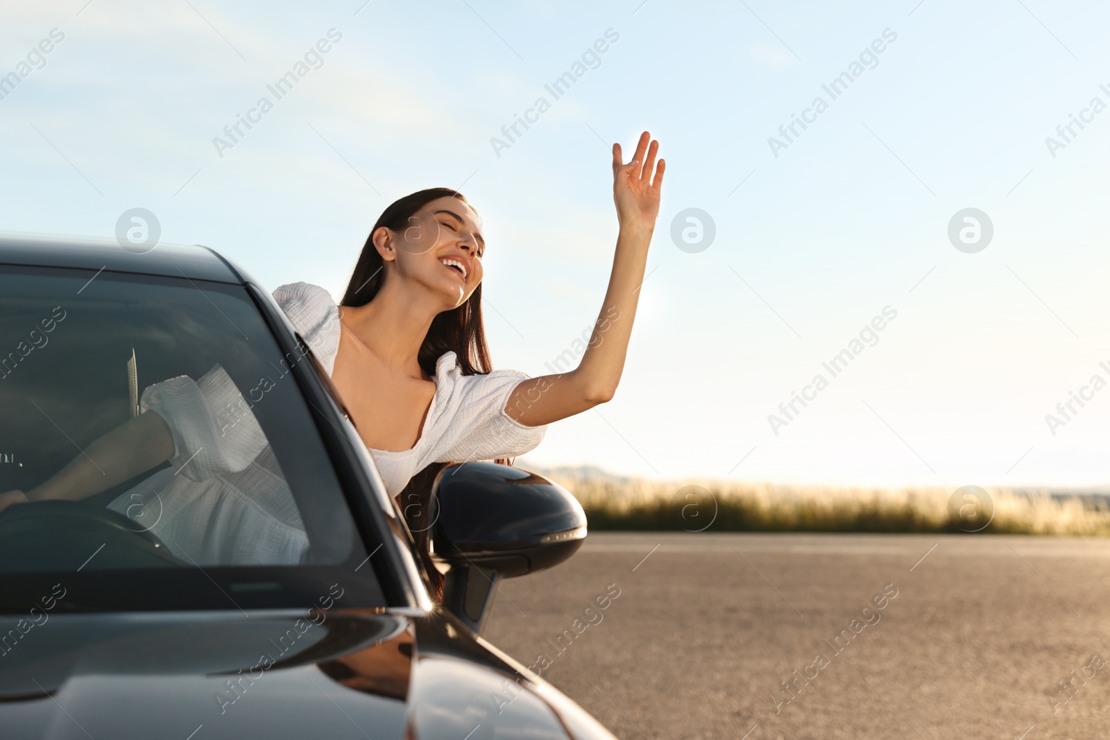 Photo of Smiling young woman leaning out of car window outdoors. Enjoying trip