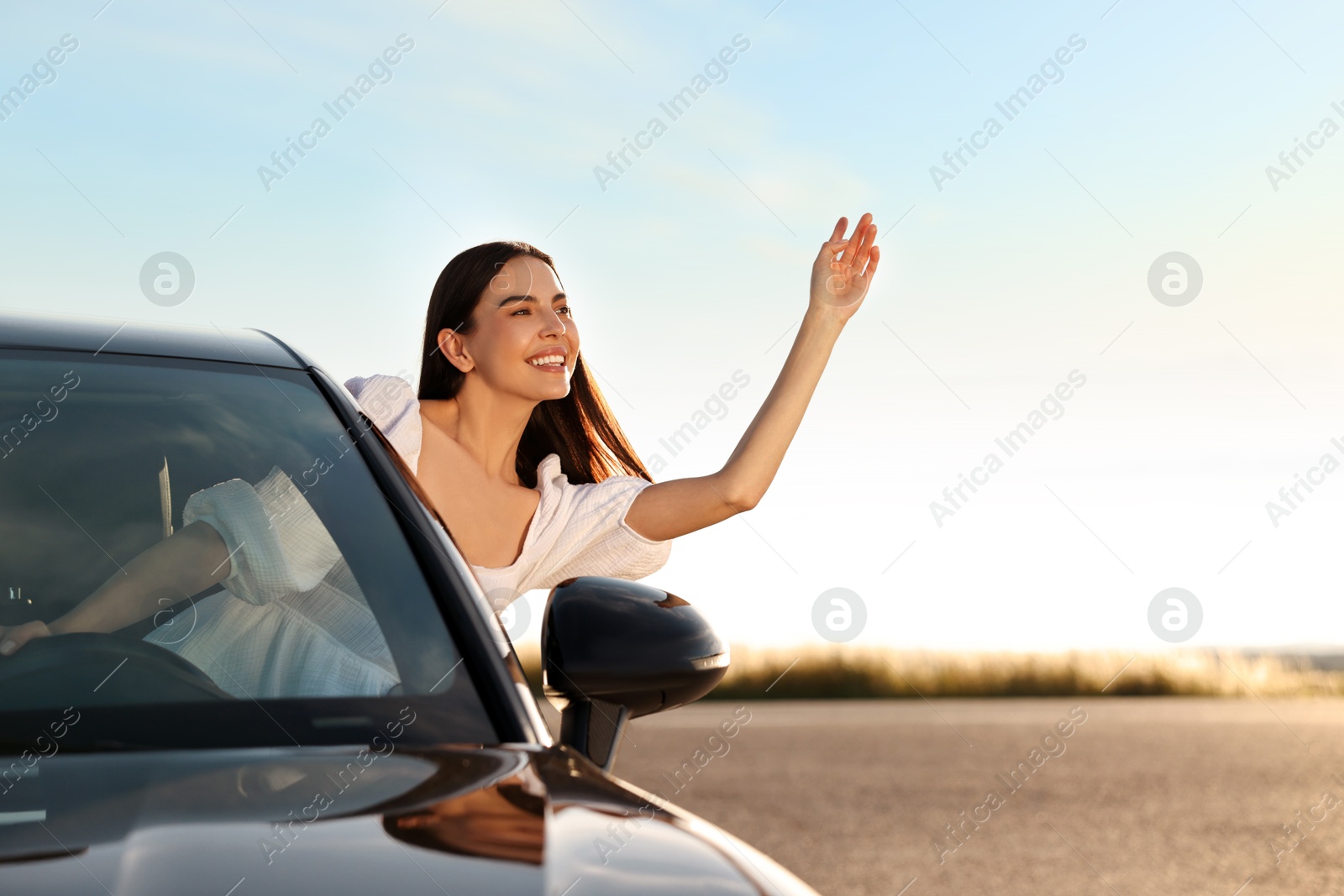 Photo of Smiling young woman leaning out of car window outdoors. Enjoying trip