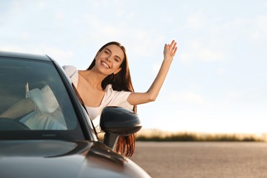 Smiling young woman leaning out of car window outdoors. Enjoying trip