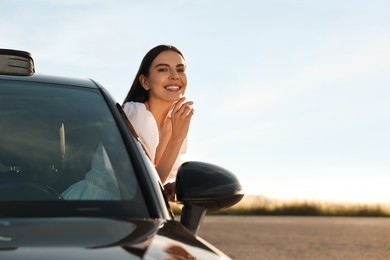 Smiling young woman leaning out of car window outdoors. Enjoying trip