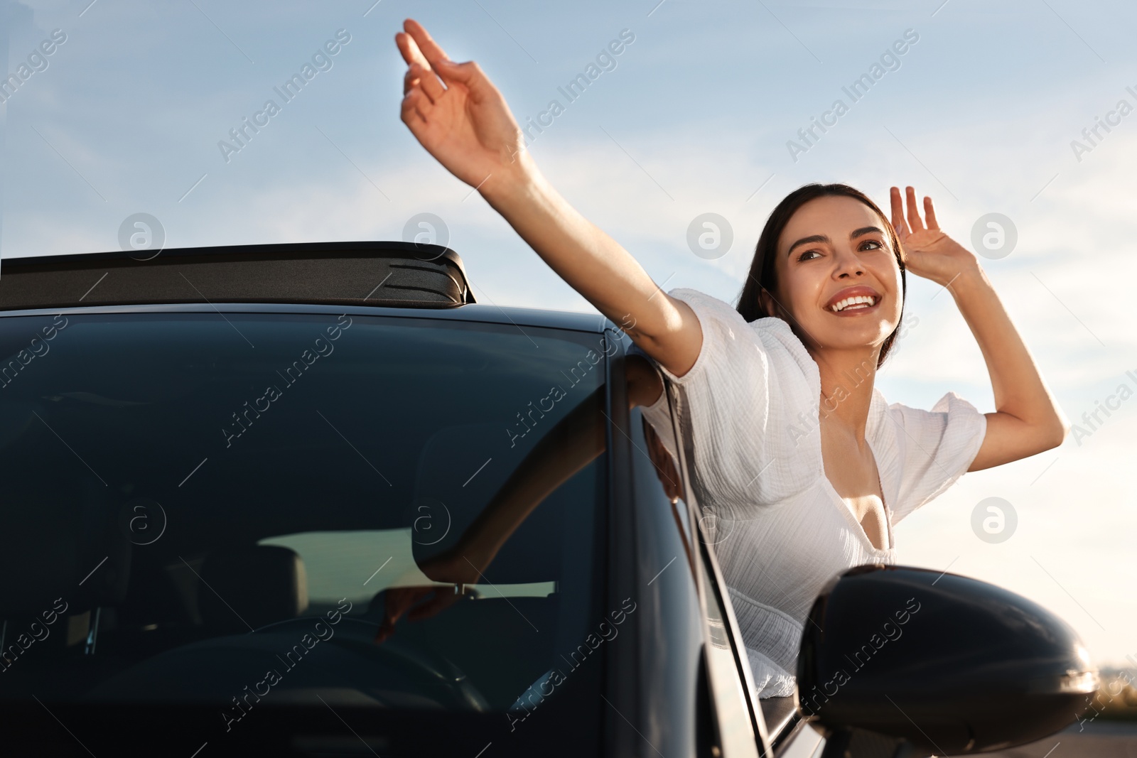 Photo of Smiling young woman leaning out of car window outdoors. Enjoying trip