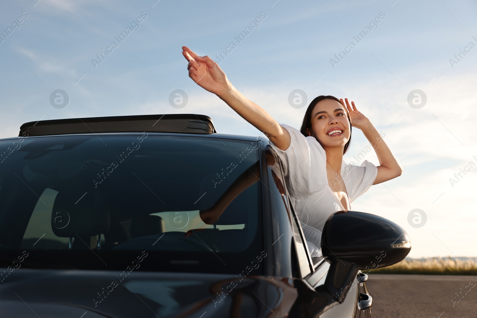 Photo of Smiling young woman leaning out of car window outdoors. Enjoying trip