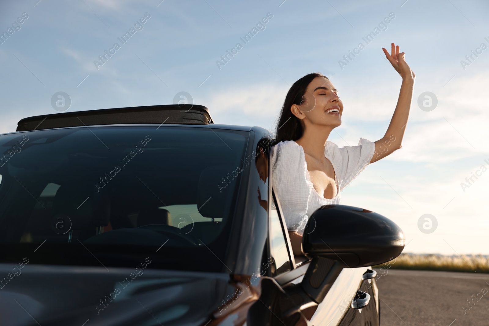 Photo of Smiling young woman leaning out of car window outdoors. Enjoying trip