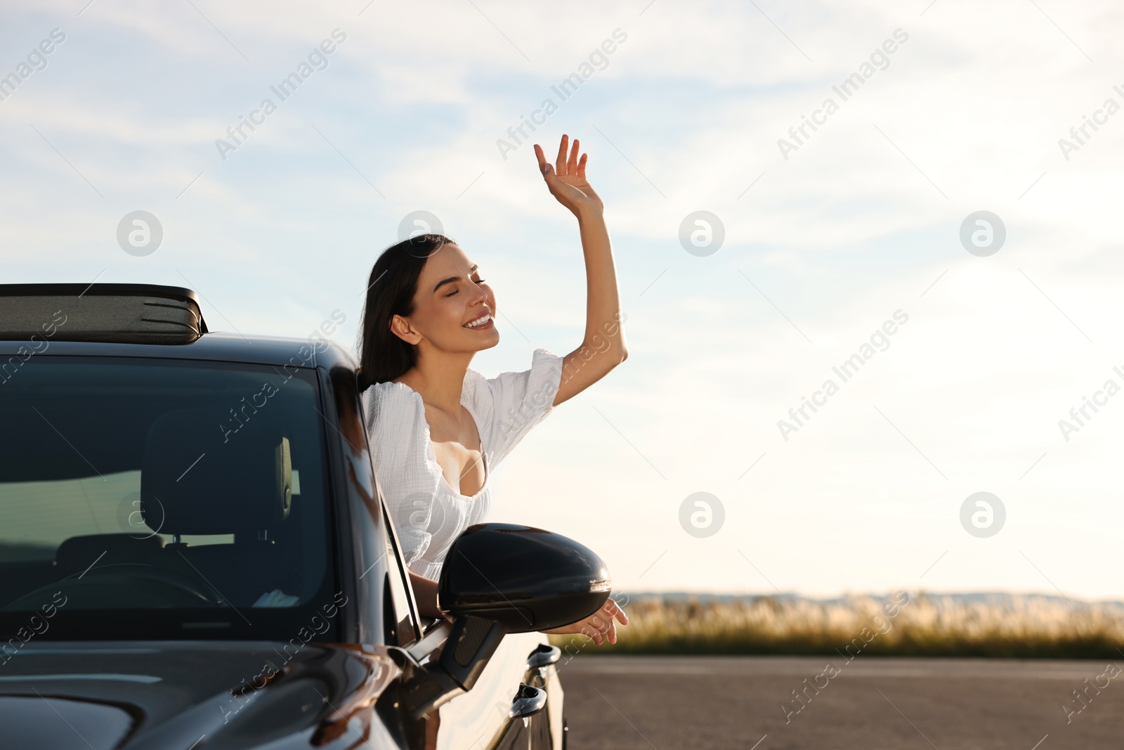 Photo of Smiling young woman leaning out of car window outdoors. Enjoying trip