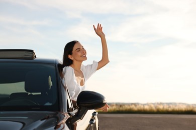 Smiling young woman leaning out of car window outdoors. Enjoying trip