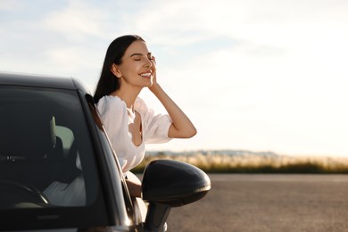 Smiling young woman leaning out of car window outdoors. Enjoying trip