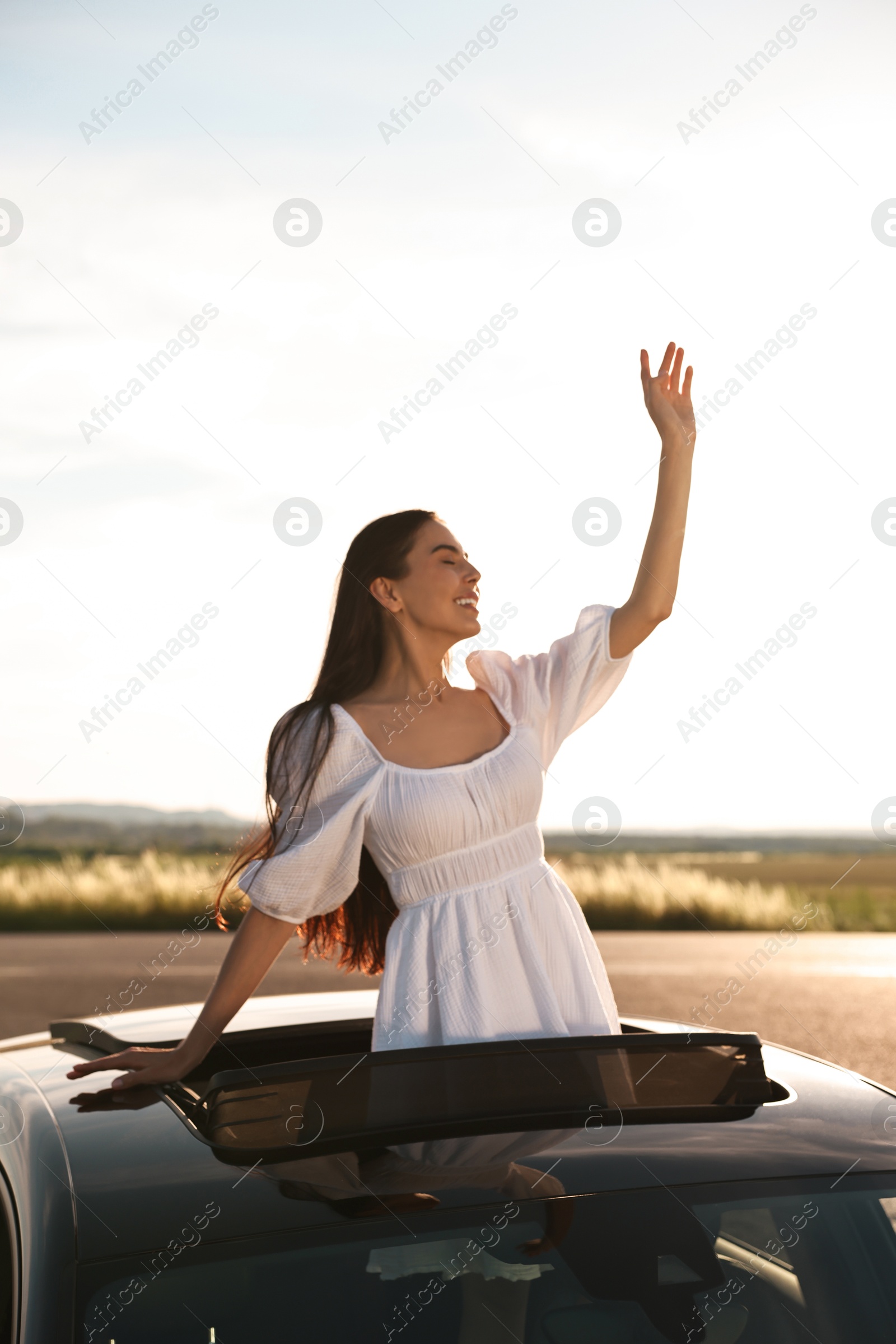 Photo of Enjoying trip. Smiling woman leaning out of car roof outdoors