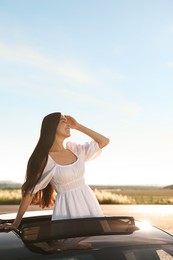 Enjoying trip. Smiling woman leaning out of car roof outdoors