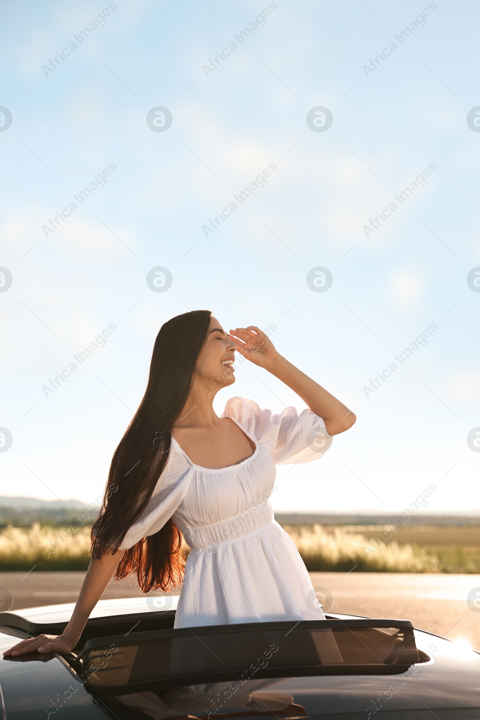 Photo of Enjoying trip. Smiling woman leaning out of car roof outdoors