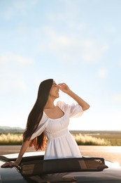 Photo of Enjoying trip. Smiling woman leaning out of car roof outdoors