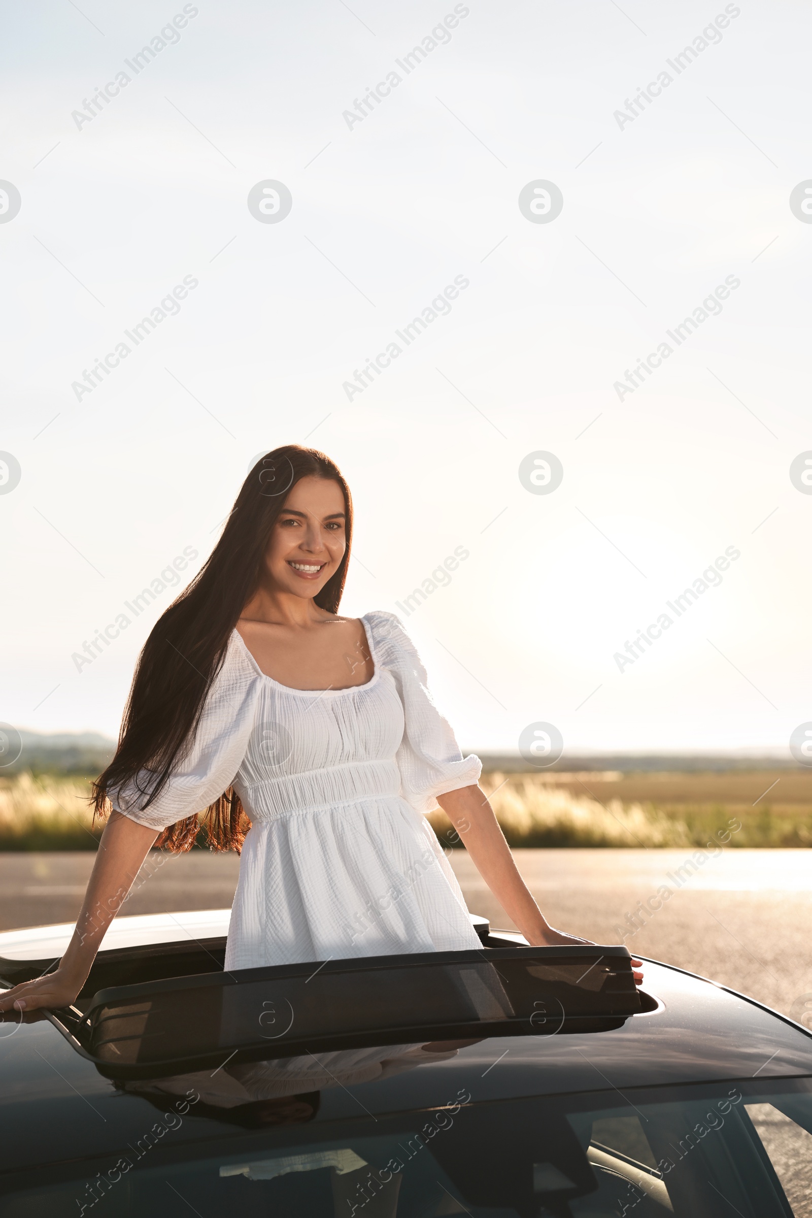 Photo of Enjoying trip. Smiling woman leaning out of car roof outdoors