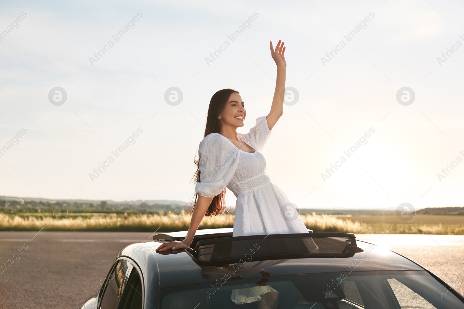 Photo of Enjoying trip. Smiling woman leaning out of car roof outdoors