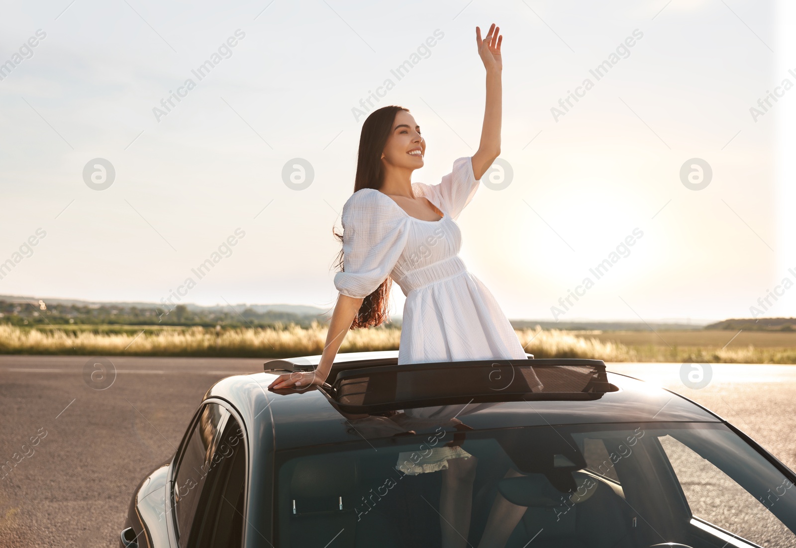 Photo of Enjoying trip. Smiling woman leaning out of car roof outdoors