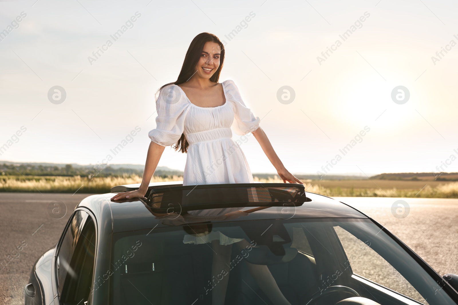 Photo of Enjoying trip. Smiling woman leaning out of car roof outdoors