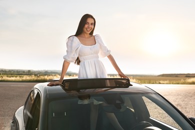 Photo of Enjoying trip. Smiling woman leaning out of car roof outdoors