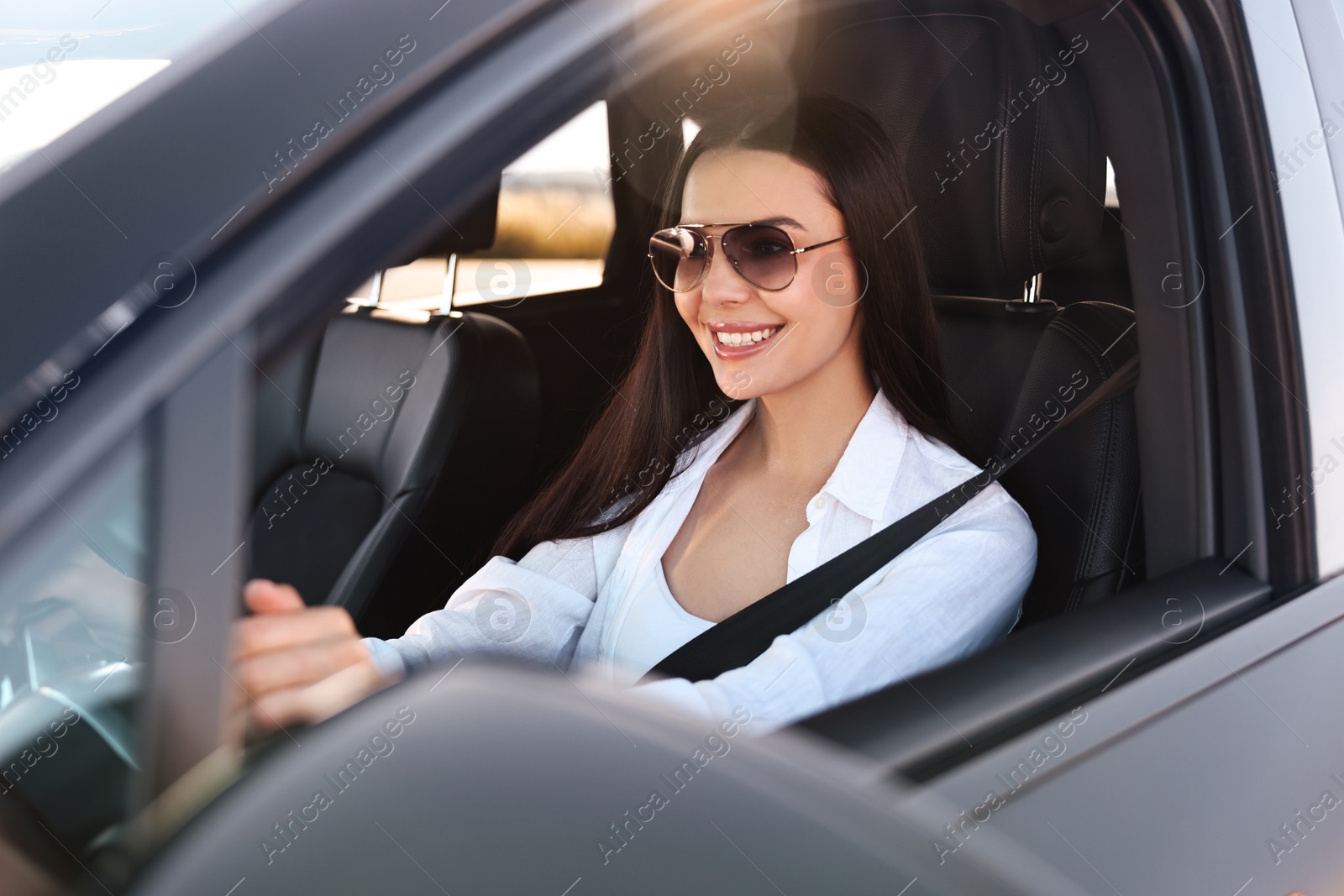 Photo of Smiling young woman in sunglasses with seatbelt driving car, view from outside