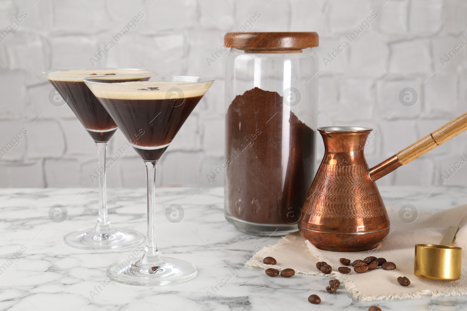 Photo of Refreshing cocktails in glasses, beans, cezve and ground coffee on white marble table