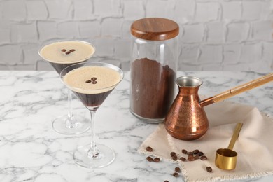 Refreshing cocktails in glasses, beans, cezve and ground coffee on white marble table