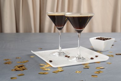 Photo of Fresh coffee cocktails in glasses, beans and confetti on grey table