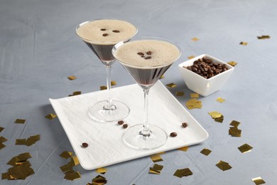 Photo of Fresh coffee cocktails in glasses, beans and confetti on grey table