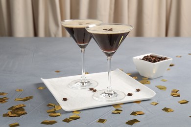 Photo of Fresh coffee cocktails in glasses, beans and confetti on grey table