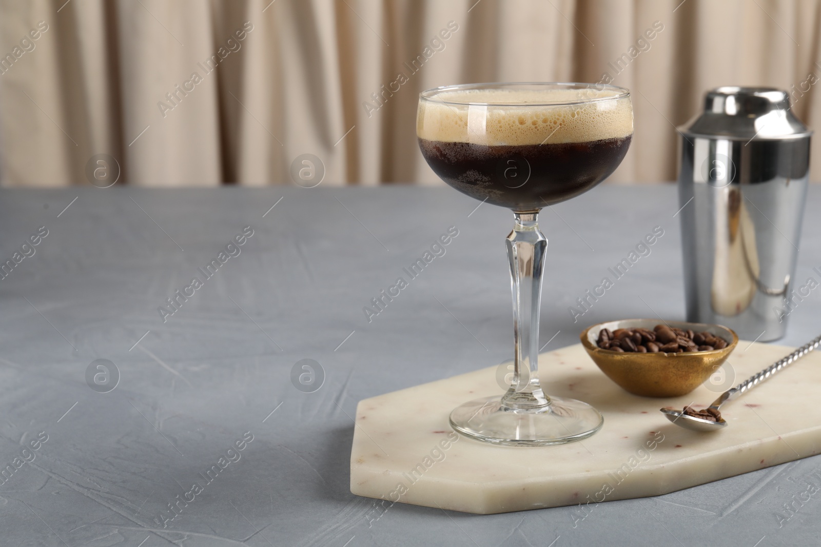 Photo of Fresh coffee cocktail in glass, beans and bartender equipment on grey table, space for text