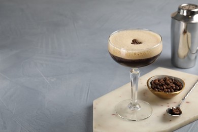 Photo of Fresh coffee cocktail in glass, beans and bartender equipment on grey table, space for text