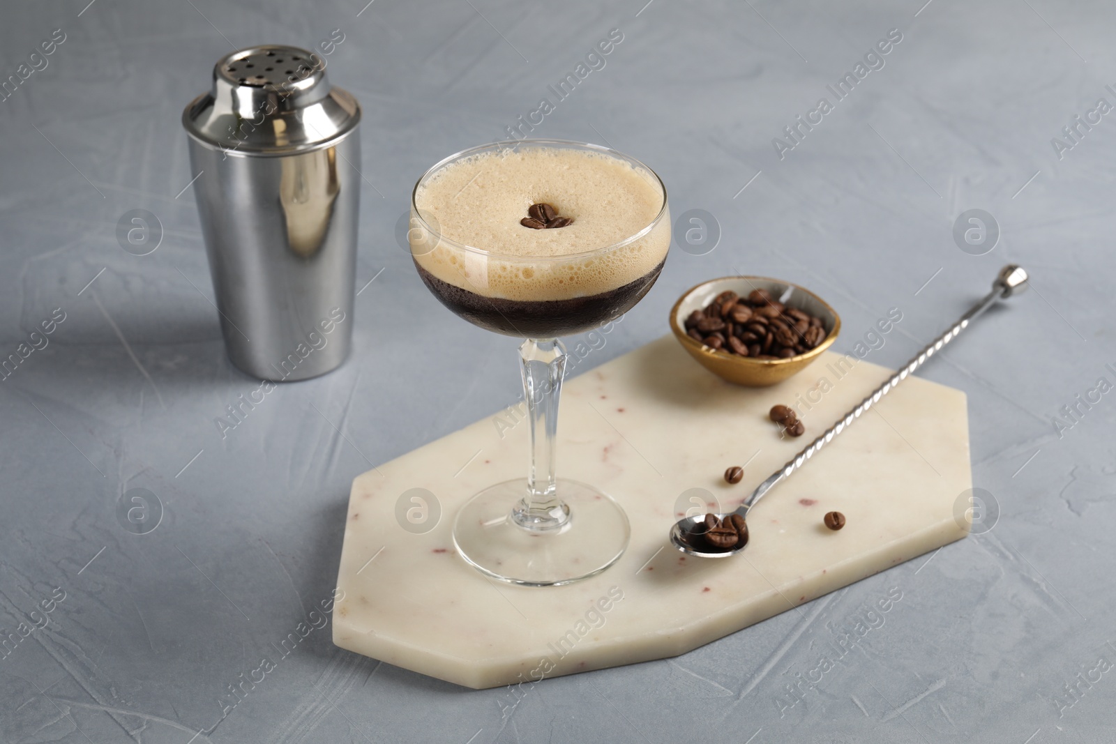 Photo of Fresh coffee cocktail in glass, beans and bartender equipment on grey table