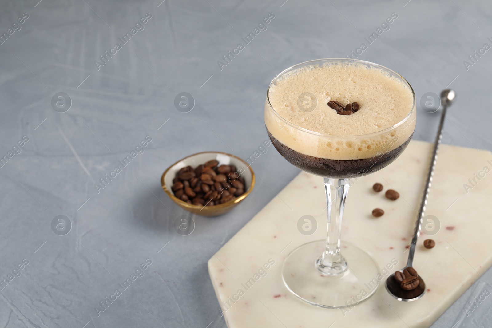 Photo of Fresh coffee cocktail in glass, beans and mixing spoon on grey table, space for text