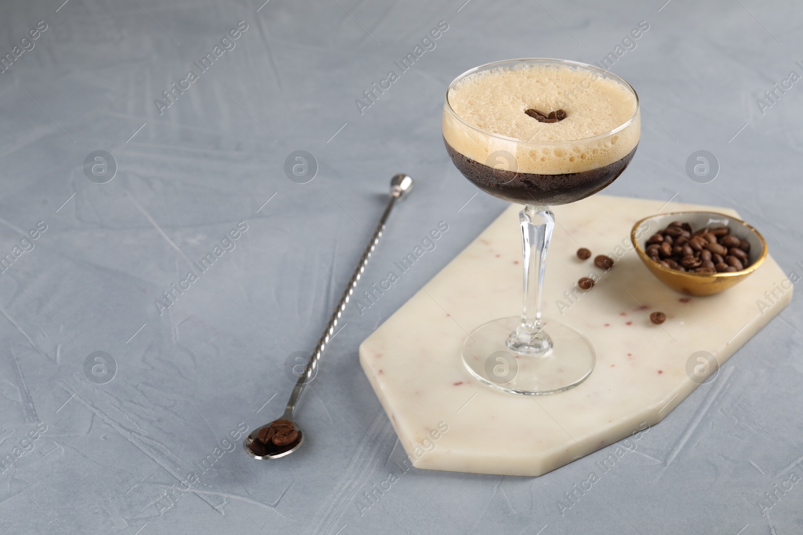 Photo of Fresh coffee cocktail in glass, beans and mixing spoon on grey table, space for text