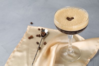 Photo of Fresh coffee cocktail in glass, beans and mixing spoon on grey table. Space for text