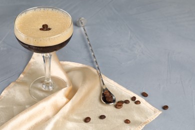 Fresh coffee cocktail in glass, beans and mixing spoon on grey table. Space for text