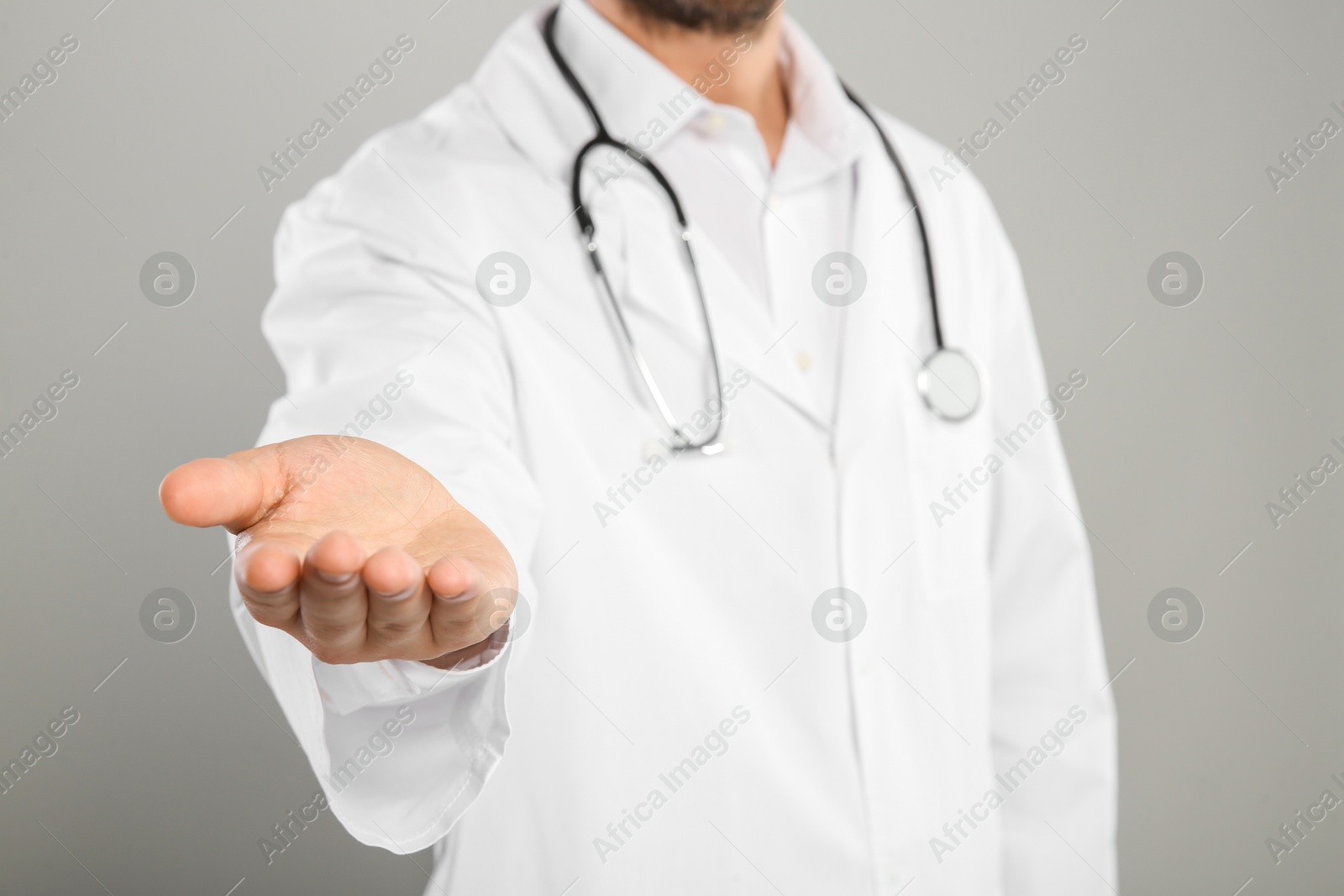 Photo of Doctor with stethoscope holding something on light grey background, closeup