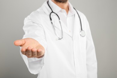 Photo of Doctor with stethoscope holding something on light grey background, closeup