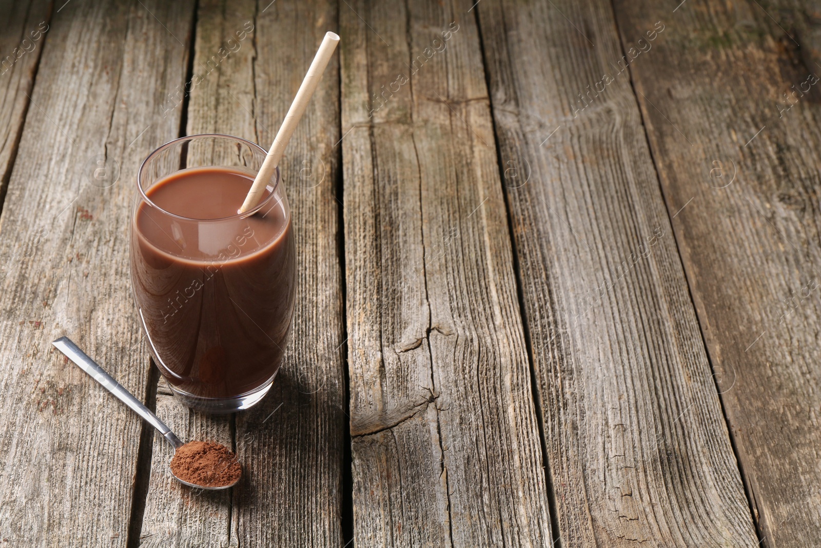 Photo of Delicious protein shake in glass and spoon with powder on wooden table, space for text