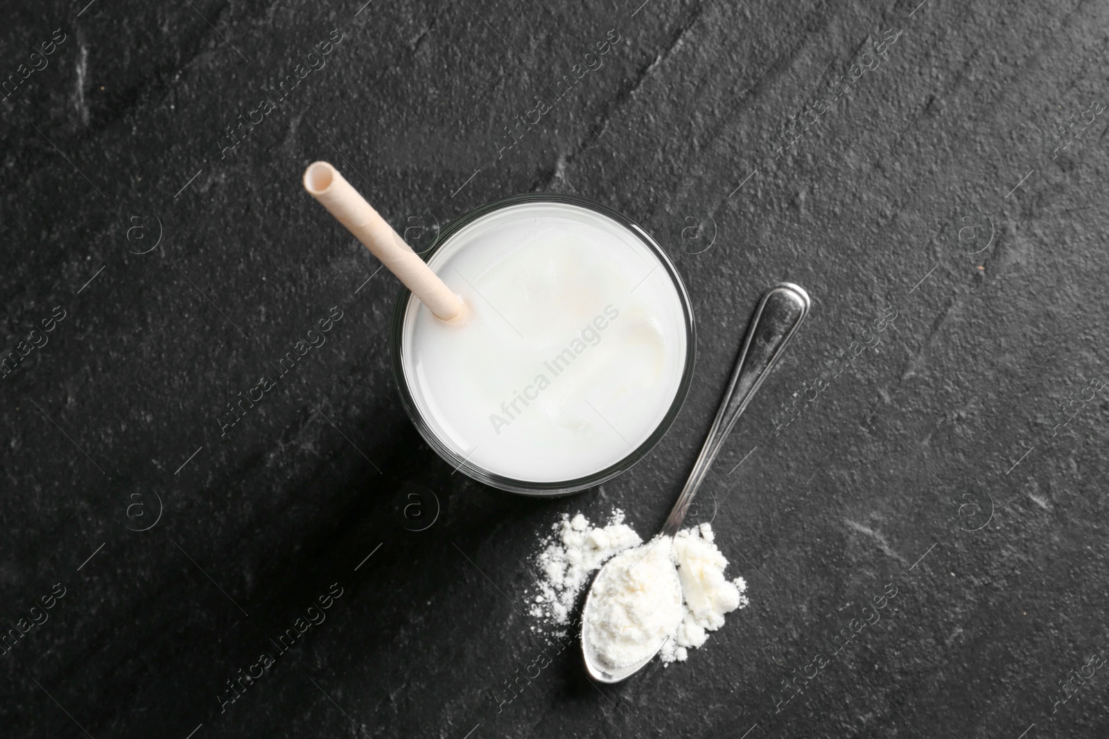 Photo of Delicious protein shake in glass and spoon with powder on black table, top view