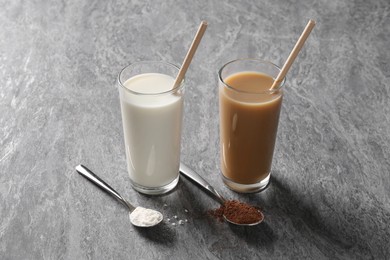 Photo of Delicious protein shakes in glasses and spoons with powder on grey table