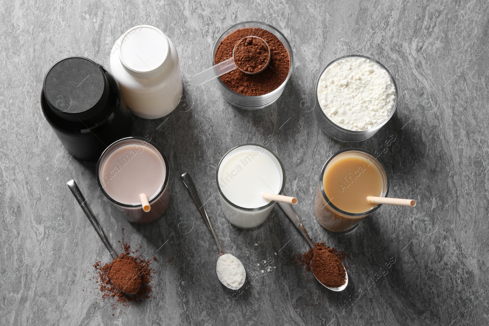 Photo of Delicious protein shakes in glasses, powder, spoons and bottles on grey table, flat lay