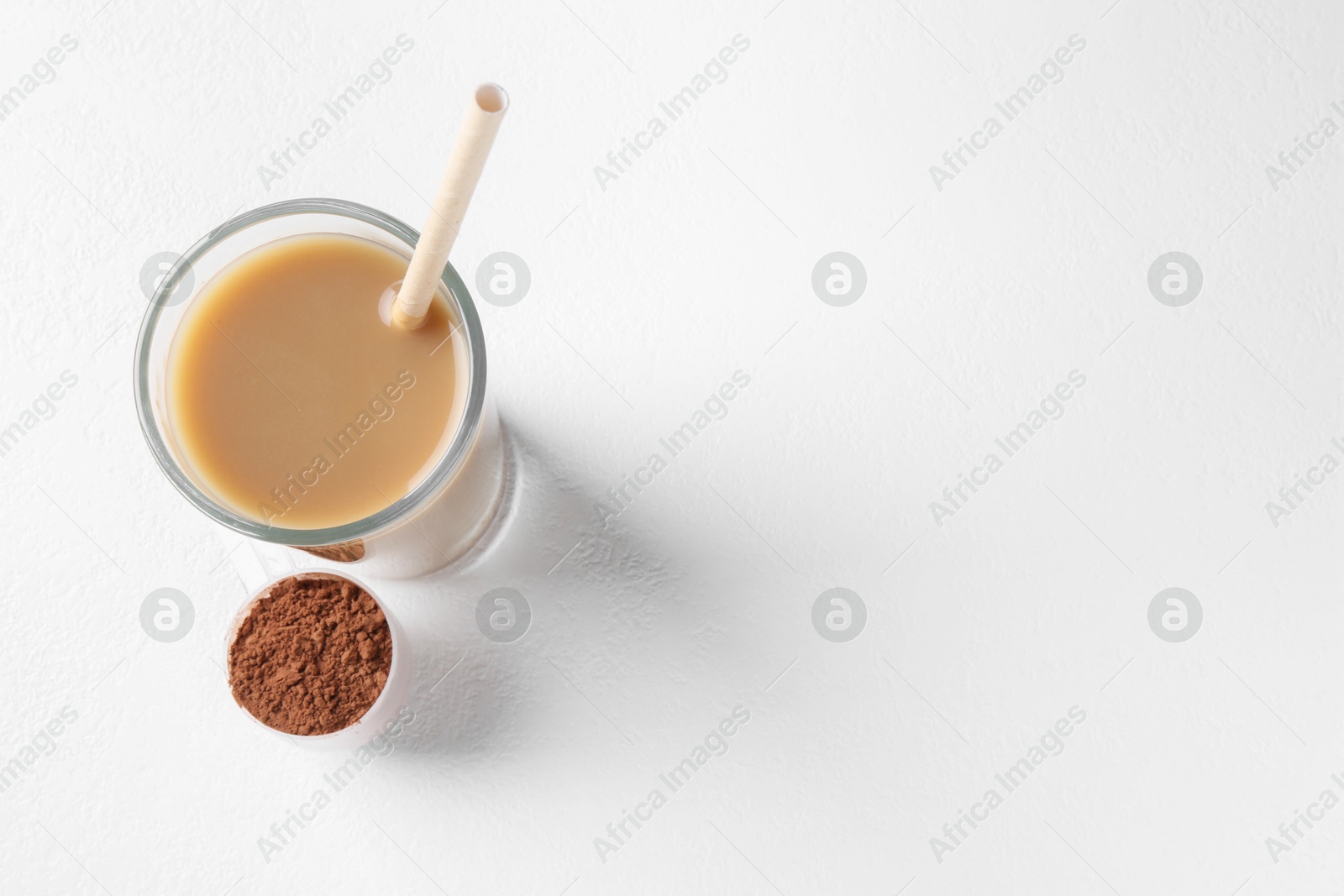 Photo of Delicious protein shake in glass and scoop with powder on white background, top view. Space for text