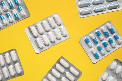 Photo of Different antibiotic pills in blisters on yellow background, flat lay