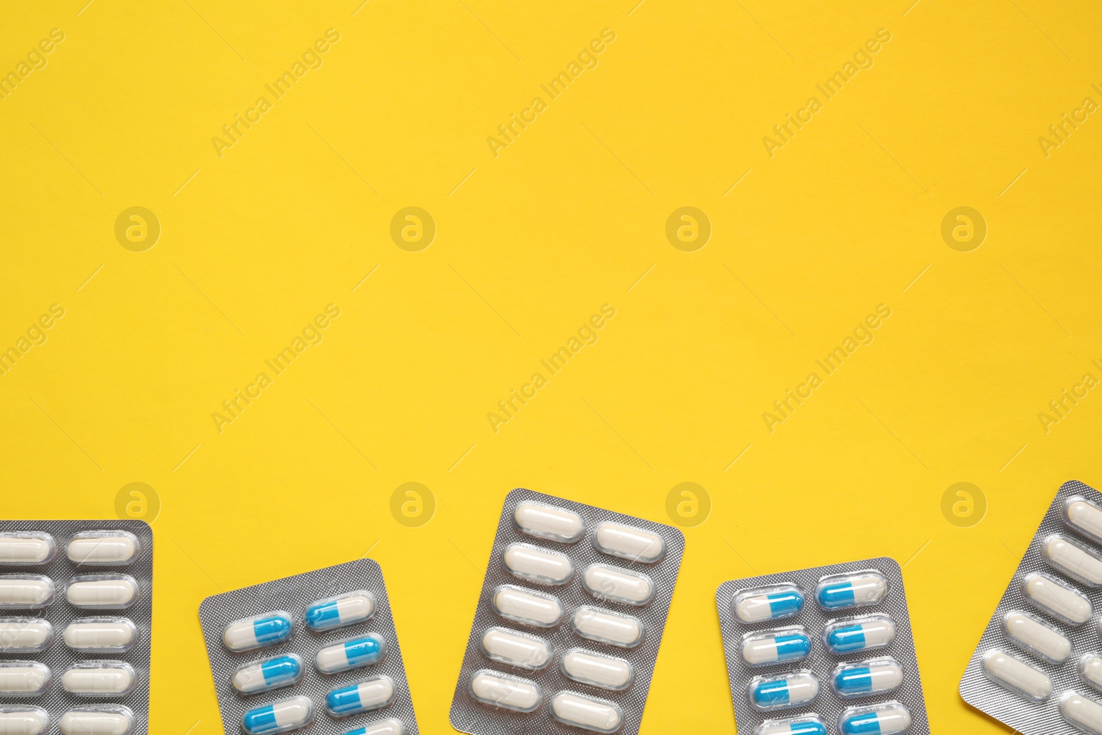 Photo of Different antibiotic pills in blisters on yellow background, flat lay. Space for text