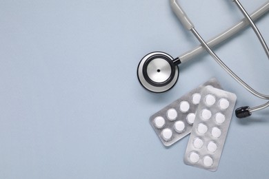 Antibiotic pills in blisters and stethoscope on gray background, flat lay. Space for text