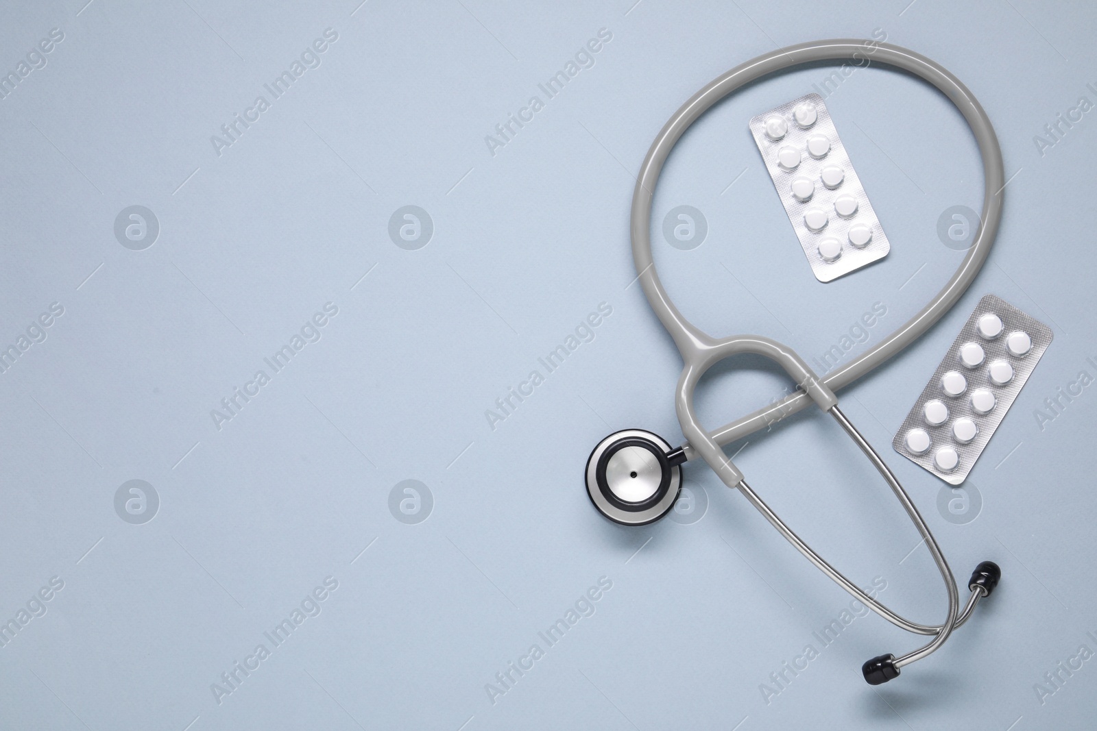 Photo of Antibiotic pills in blisters and stethoscope on gray background, flat lay. Space for text