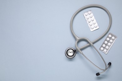 Antibiotic pills in blisters and stethoscope on gray background, flat lay. Space for text